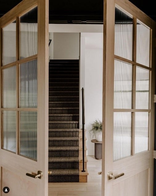 Inline image showing wooden doors opening to a large wooden staircase in an organic modern home.