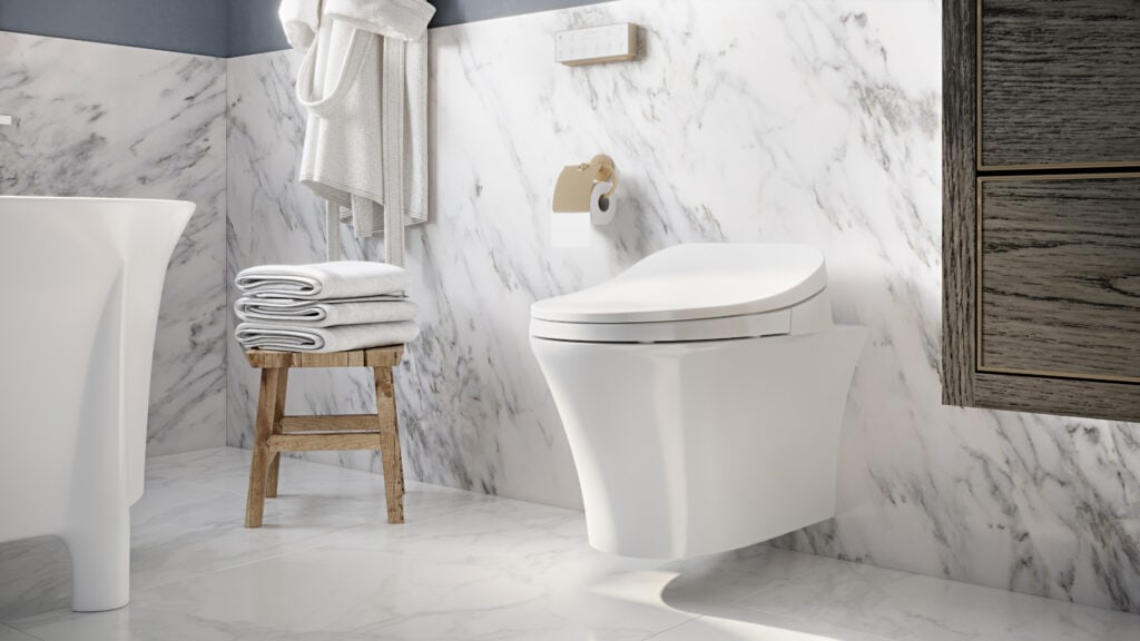 Inline image showing an Icera toilet and Vanity in a modern bathroom with natural wood floating cabinet, white marble tile on the floor and walls and a standalone bathtub.